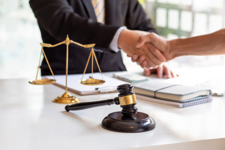 employer-defense-lawyer-winston-salem Two people shaking hands over a desk with a wooden gavel in Winston-Salem.